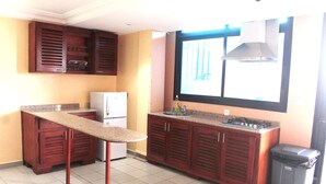 A kitchen with wooden cabinets, a granite countertop, a stainless steel range hood, and a trash bin.