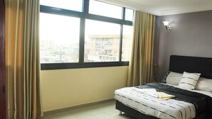 A hotel room with a large window, a bed, and a view of a building outside.