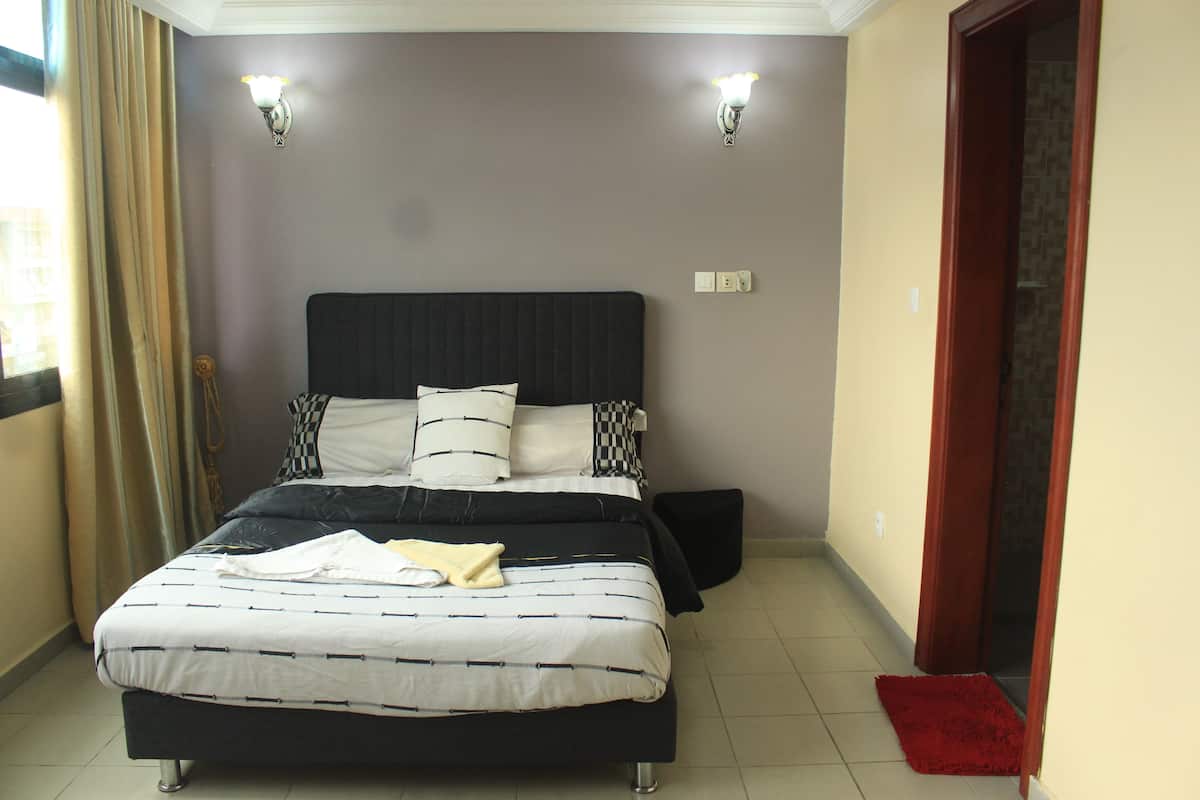 A bedroom with a bed, two wall-mounted lights, a red rug, and a door.