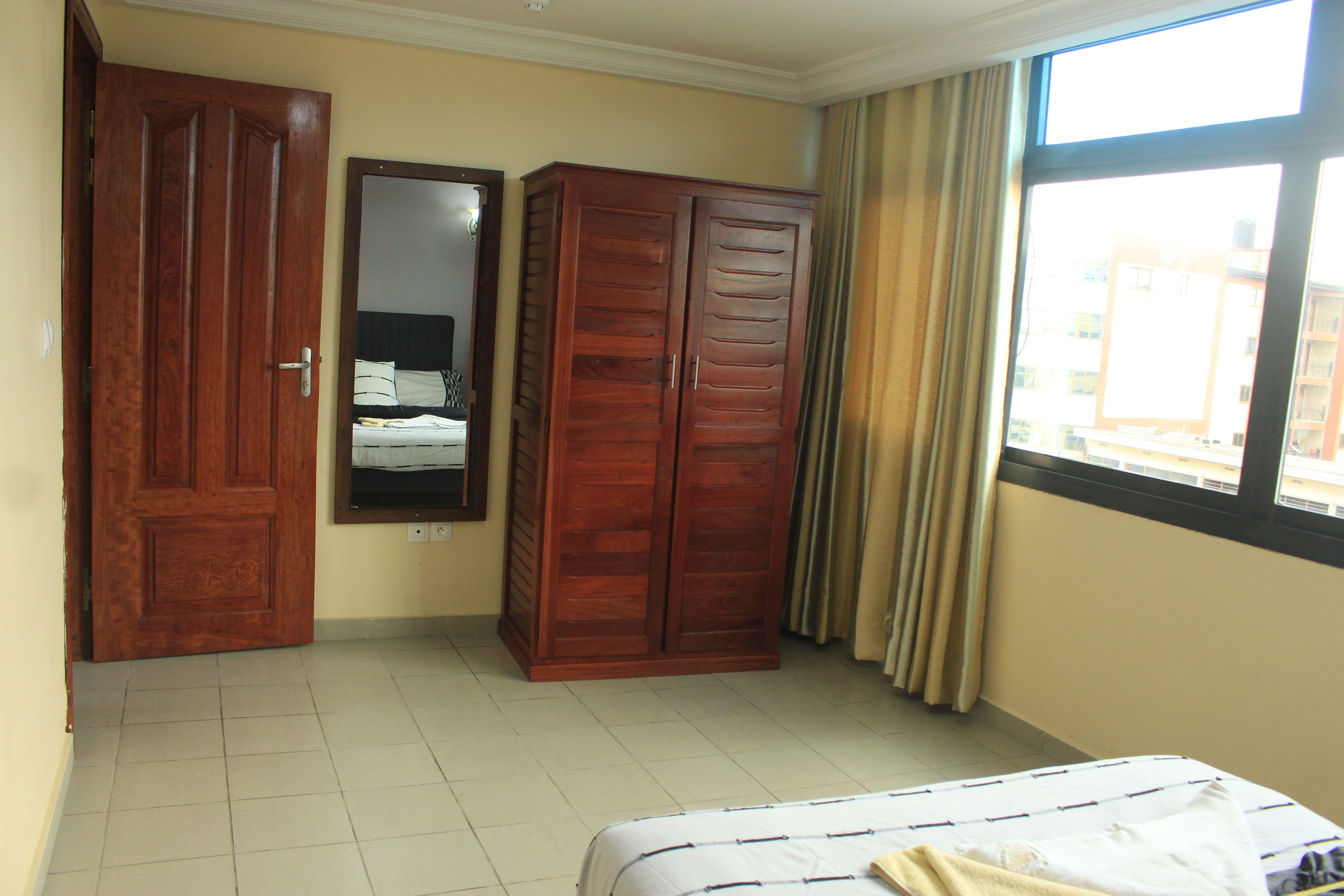 A bedroom with a bed, a wardrobe, a mirror, and a window with curtains.
