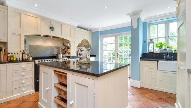 Une cuisine dotée d’un îlot central, de meubles blancs et d’une statue de Bouddha.