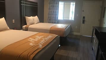 A hotel room with two beds, a large window with curtains, a door, and a small desk.
