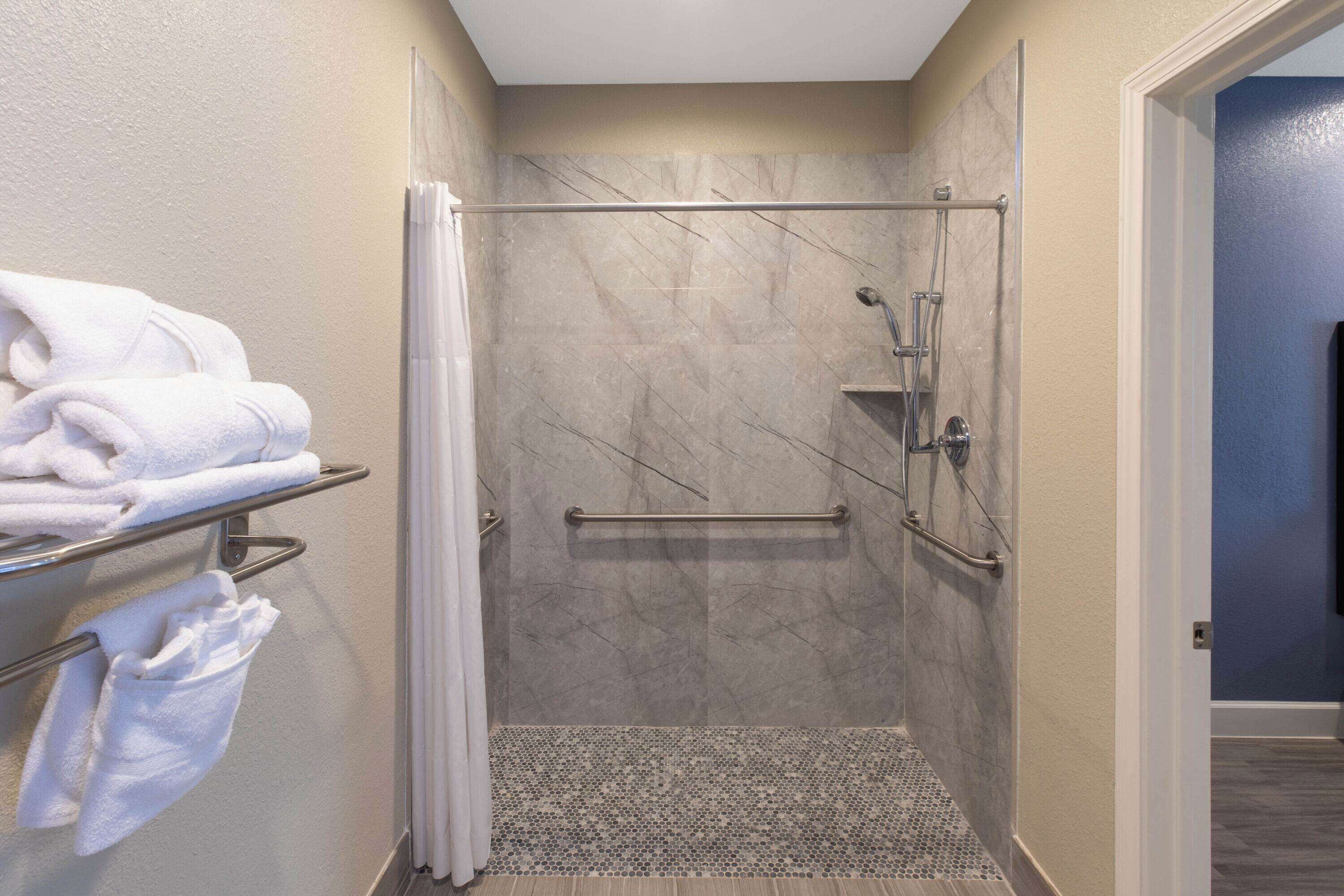 A walk-in shower with a glass door, a towel rack with folded towels, and a shower control panel.