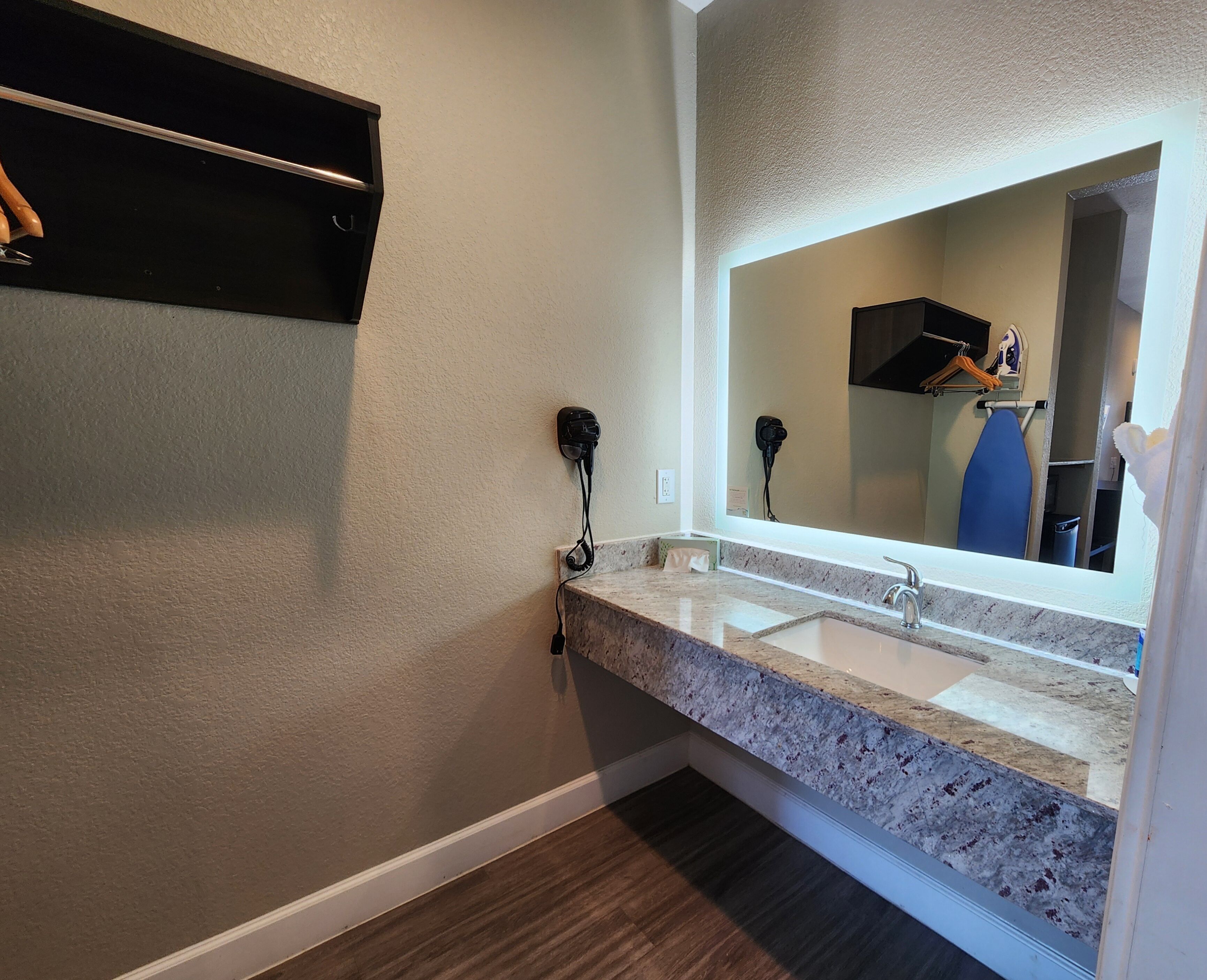 A bathroom with a marble countertop, a sink, and a mirror. There is a hairdryer plugged in on the wall.