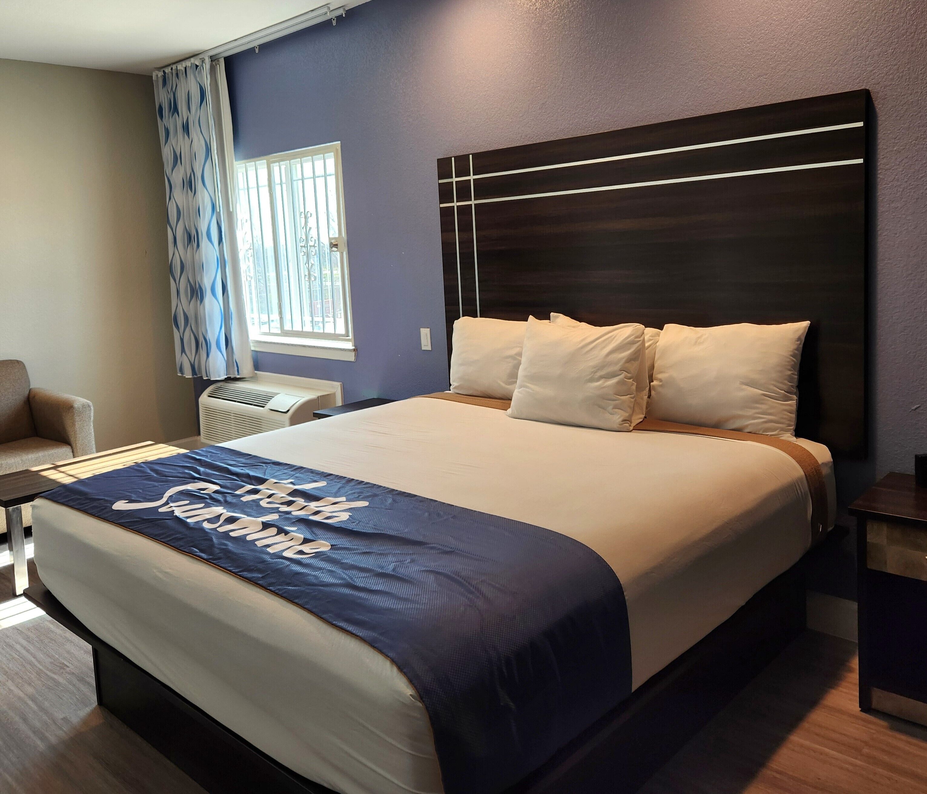 Habitación de hotel con cama, una silla, ventana con cortinas y aire acondicionado de pared.