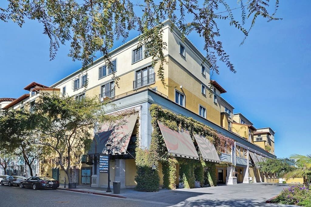 Un hotel a più piani con facciata gialla, ampie tende da sole e un'area di parcheggio con auto.