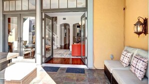 A modern interior with a glass door entrance, a seating area with a sofa and cushions, and a visible kitchen area in the background.