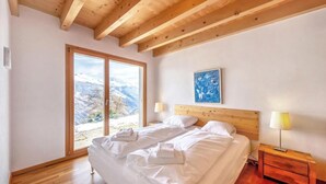 A bedroom with a wooden ceiling, a large bed with white linens, a nightstand with a lamp, and a painting on the wall. - Chalet, wifi, ski-in/ski-out & foot of the slopes, sauna, terrace, balcony, fireplace or stove (Les Collons)