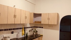 A modern kitchen with light wood cabinets, a black countertop, and a checkered floor mat. - A perfect home for a stay in Electronic City... (Bangalore)