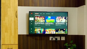 A flat-screen TV mounted on a wooden wall with a wooden cabinet below. - A perfect home for a stay in Electronic City... (Bangalore)