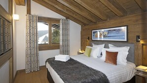 A bedroom with a bed, pillows, a blanket, a window with curtains, a painting on the wall, and a wooden ceiling.