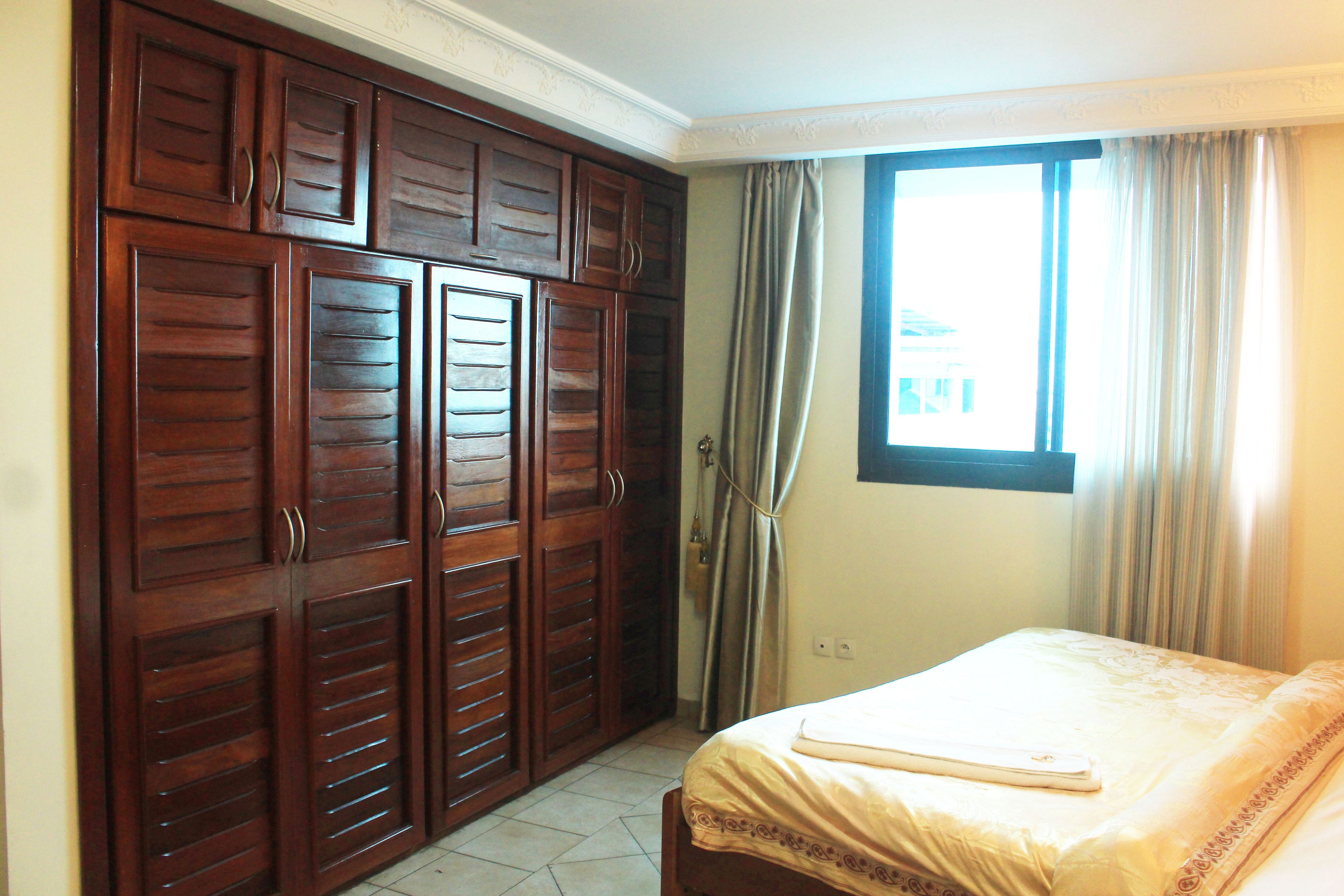 A bedroom with a bed, a window with curtains, and a wardrobe.