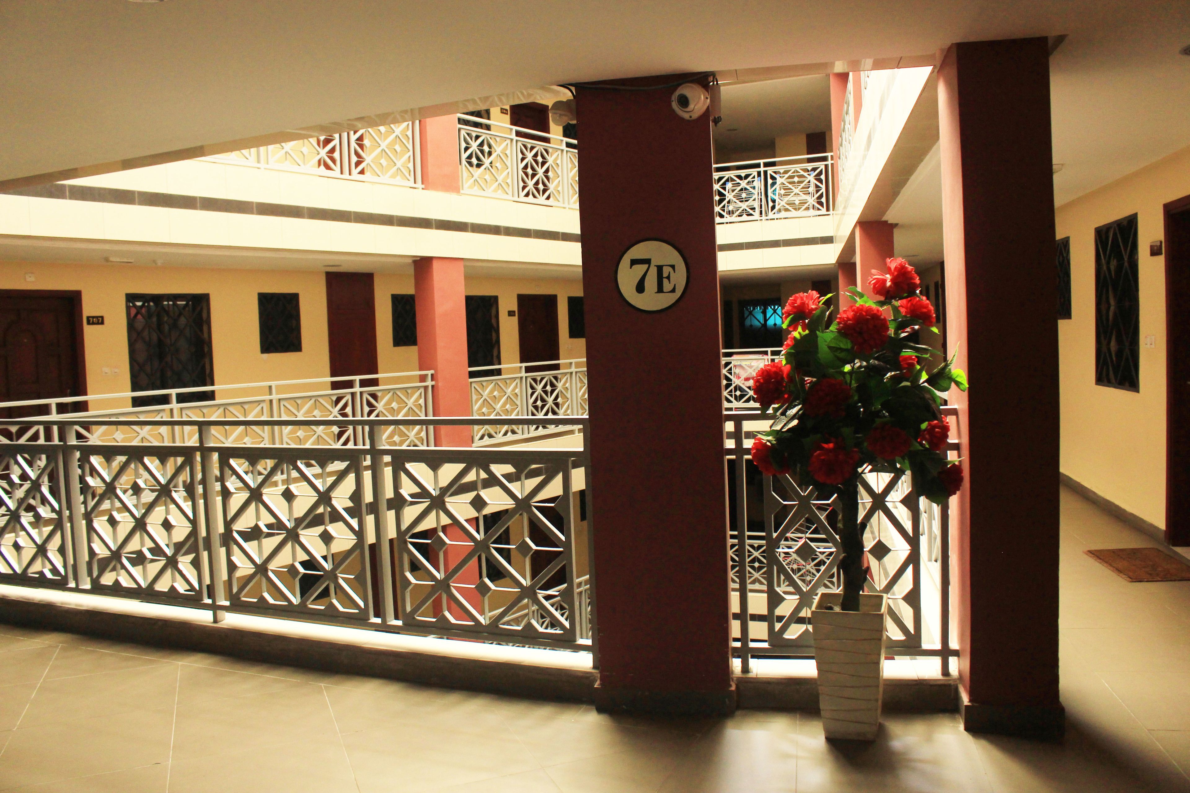 A multi-level atrium with a decorative railing, a column marked with the number 7E, and a potted plant with red flowers.