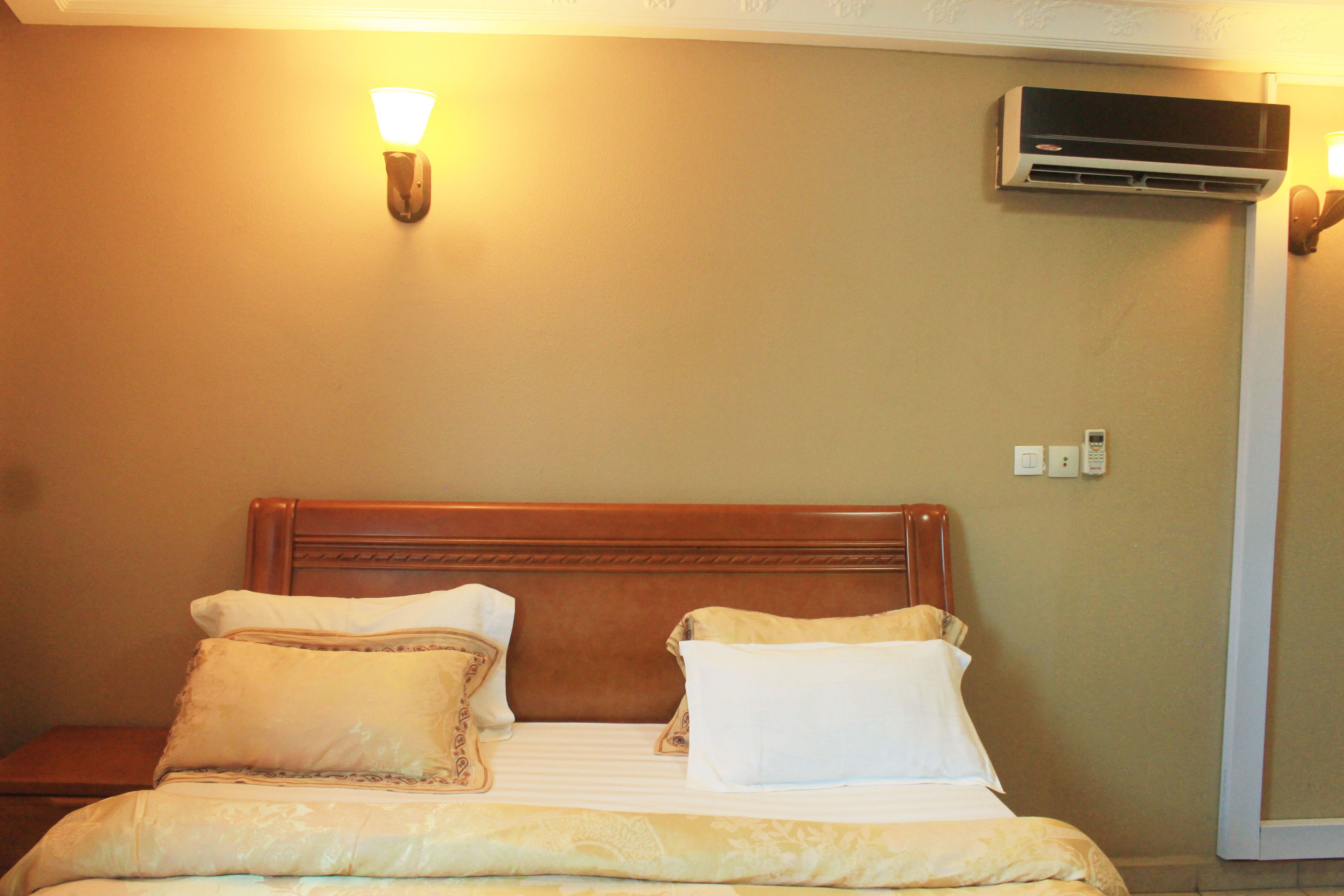 A neatly made bed with a wooden headboard, two bedside tables, and a wall-mounted air conditioner.