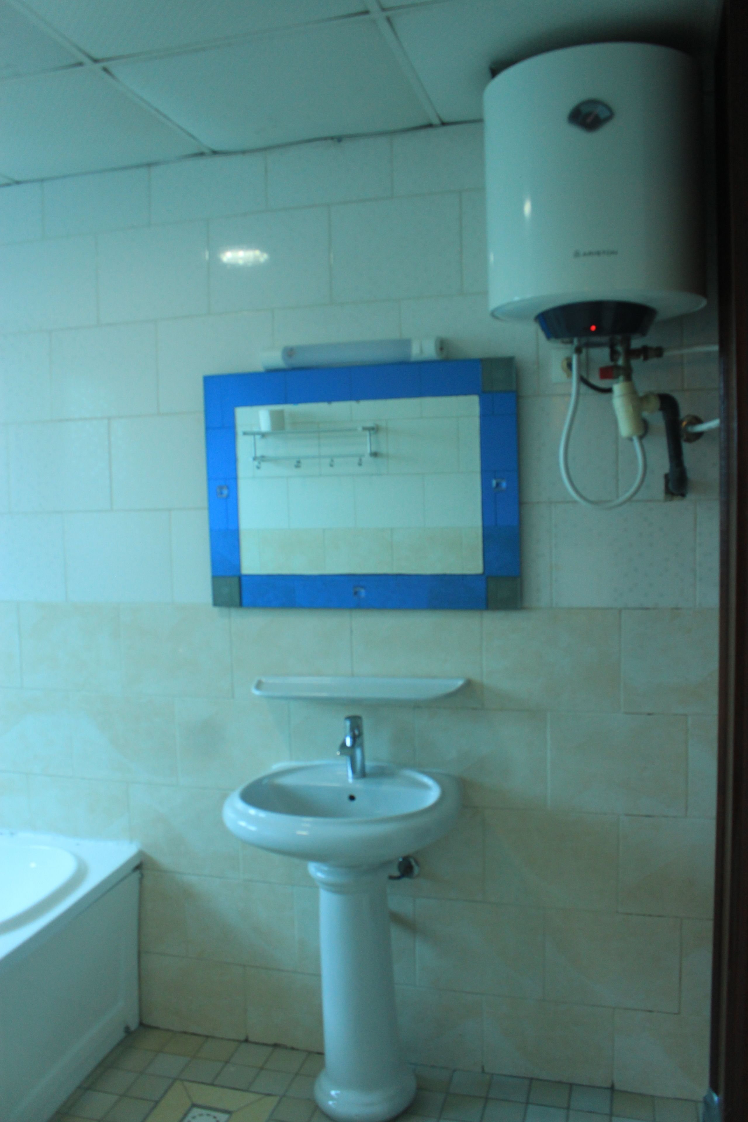 A bathroom with a pedestal sink, a bathtub, and a wall-mounted heater.