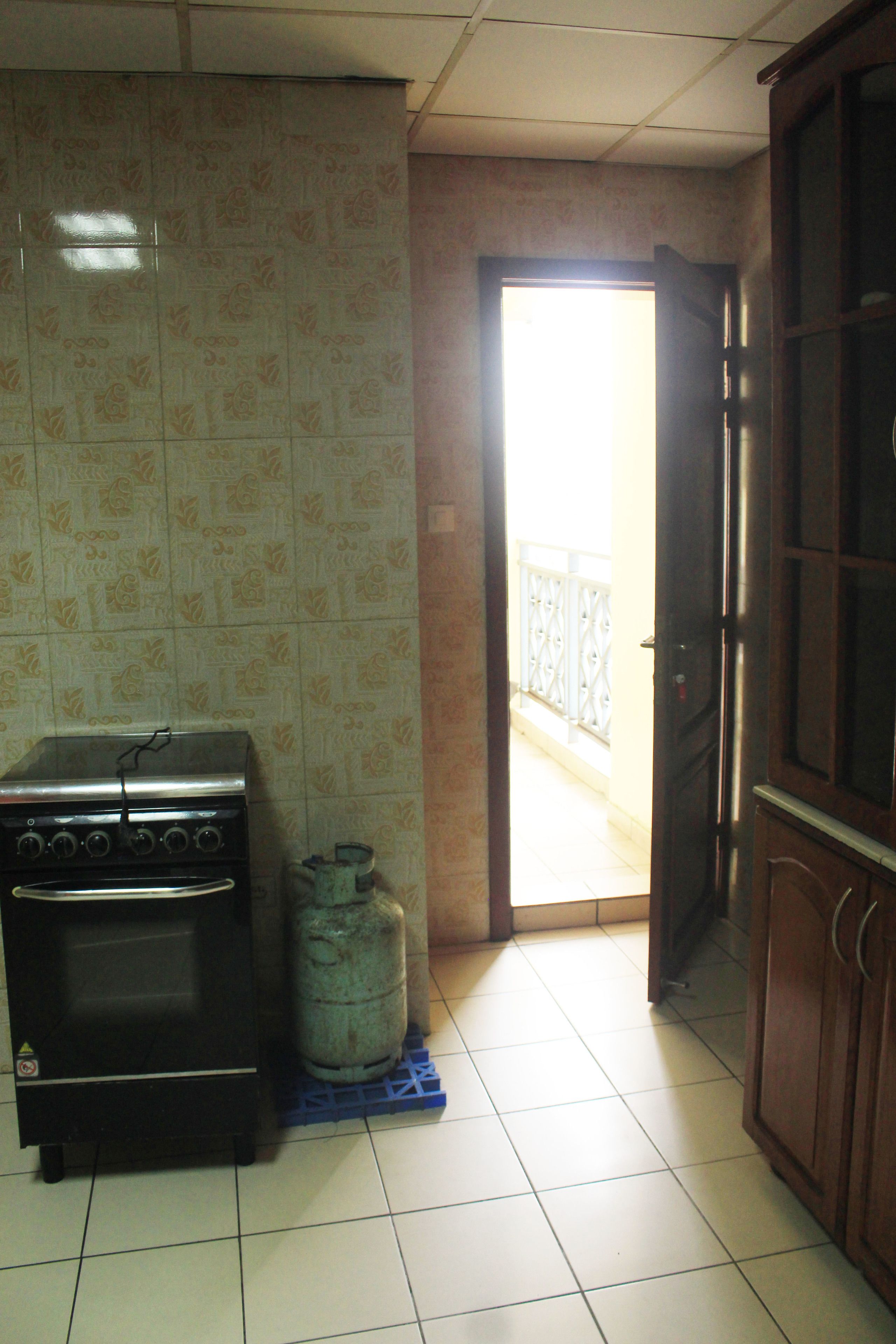 A kitchen with a gas stove, a gas cylinder, and a cabinet.