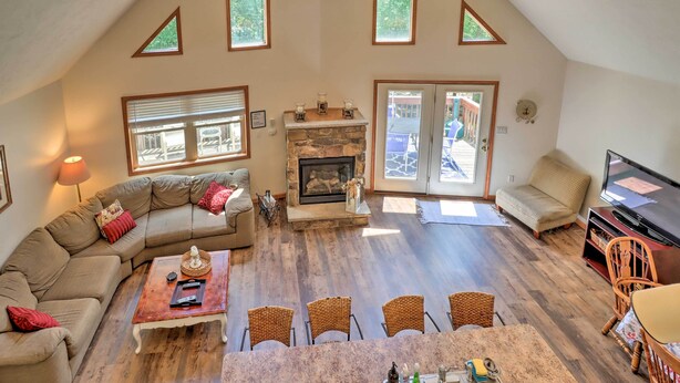 A spacious living room with a stone fireplace, a large TV, and a dining area with wicker chairs. - Deck, Hot Tub & Game Room: Lake Harmony Home (Lake Harmony)