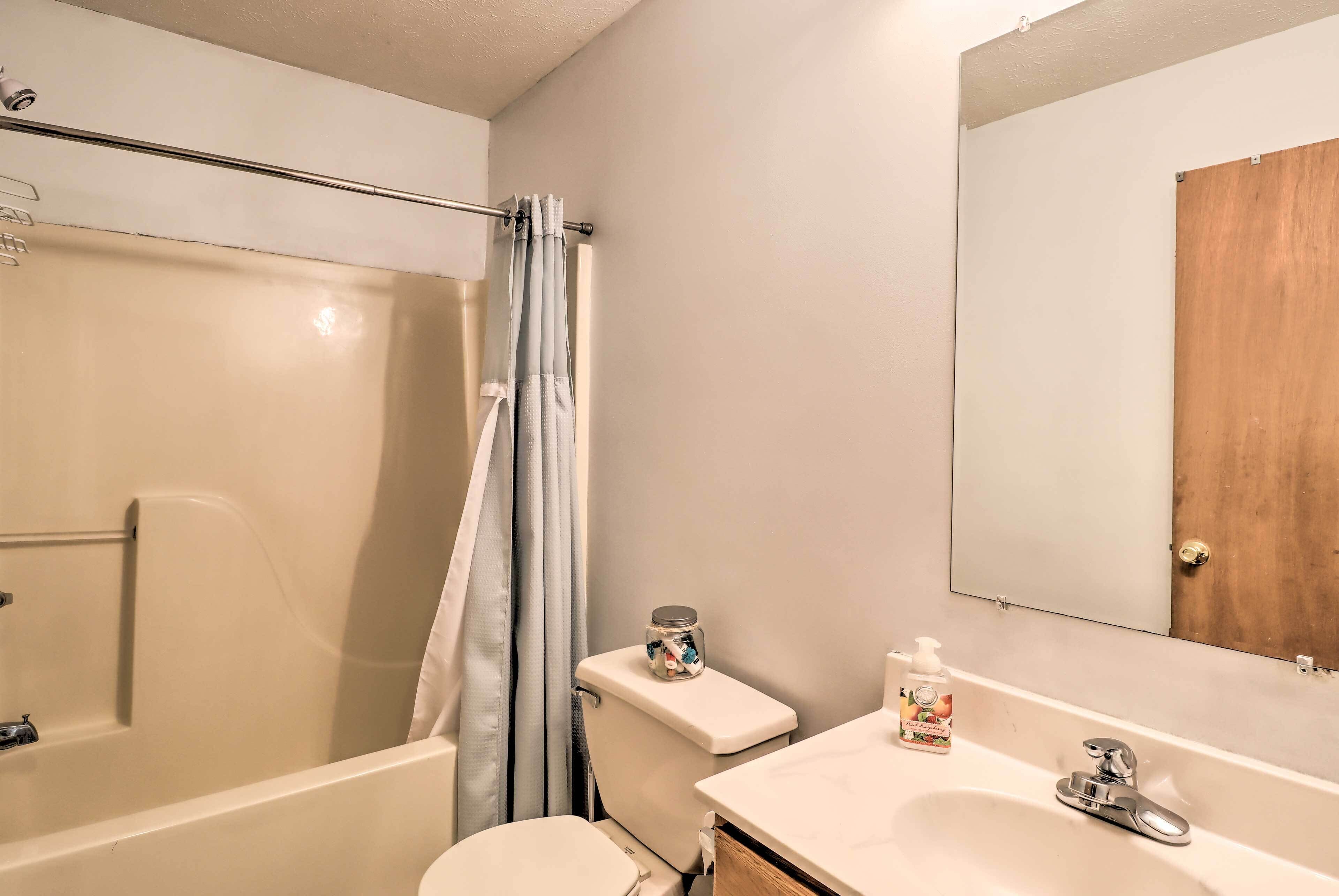 A bathroom with a bathtub, toilet, shower curtain, and a sink with a mirror above it.