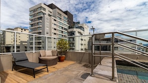 Une terrasse sur le toit avec une piscine, des chaises longues et un pot de fleurs.