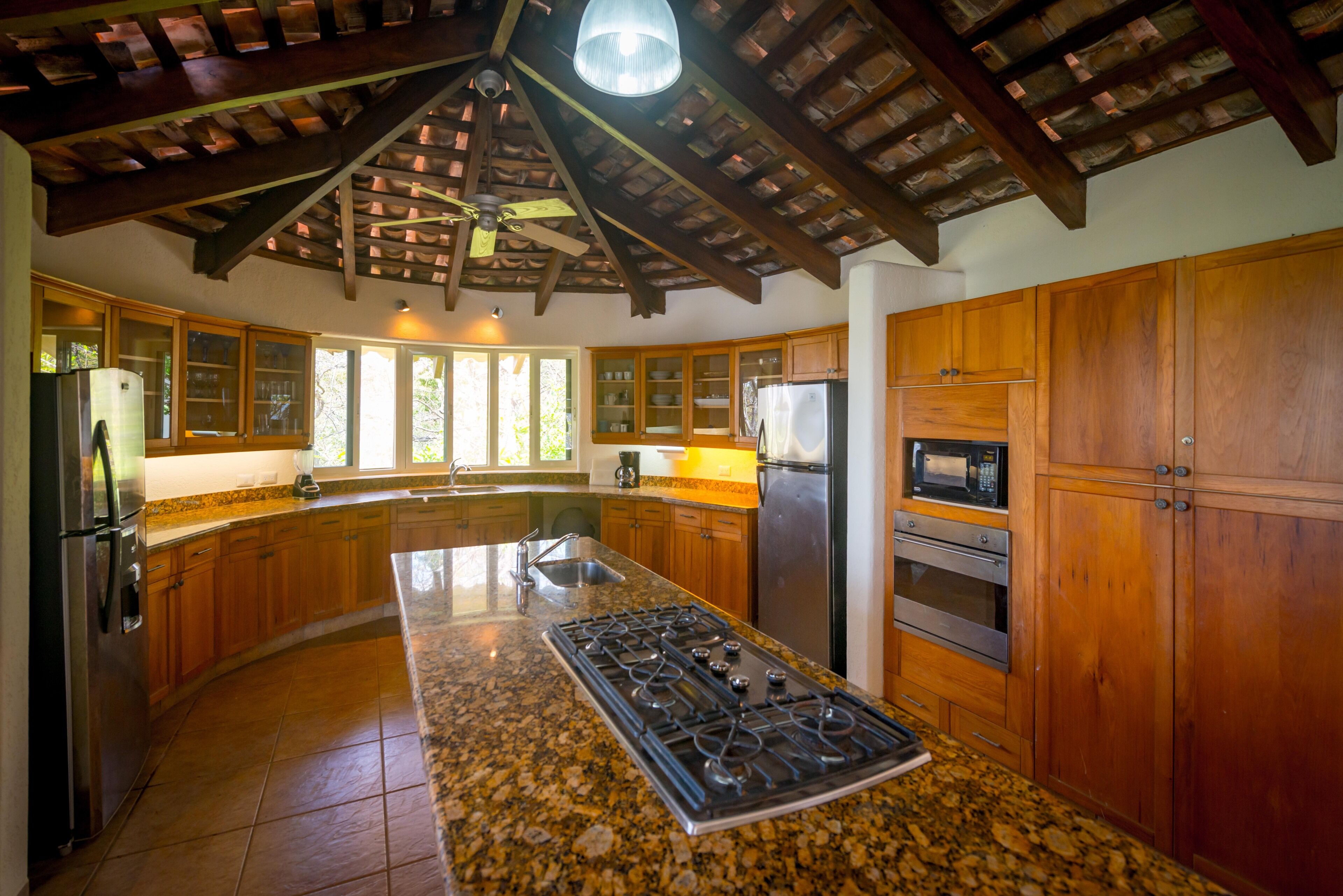 A kitchen with wooden cabinets, a granite countertop, a gas stove, a refrigerator, and a microwave.