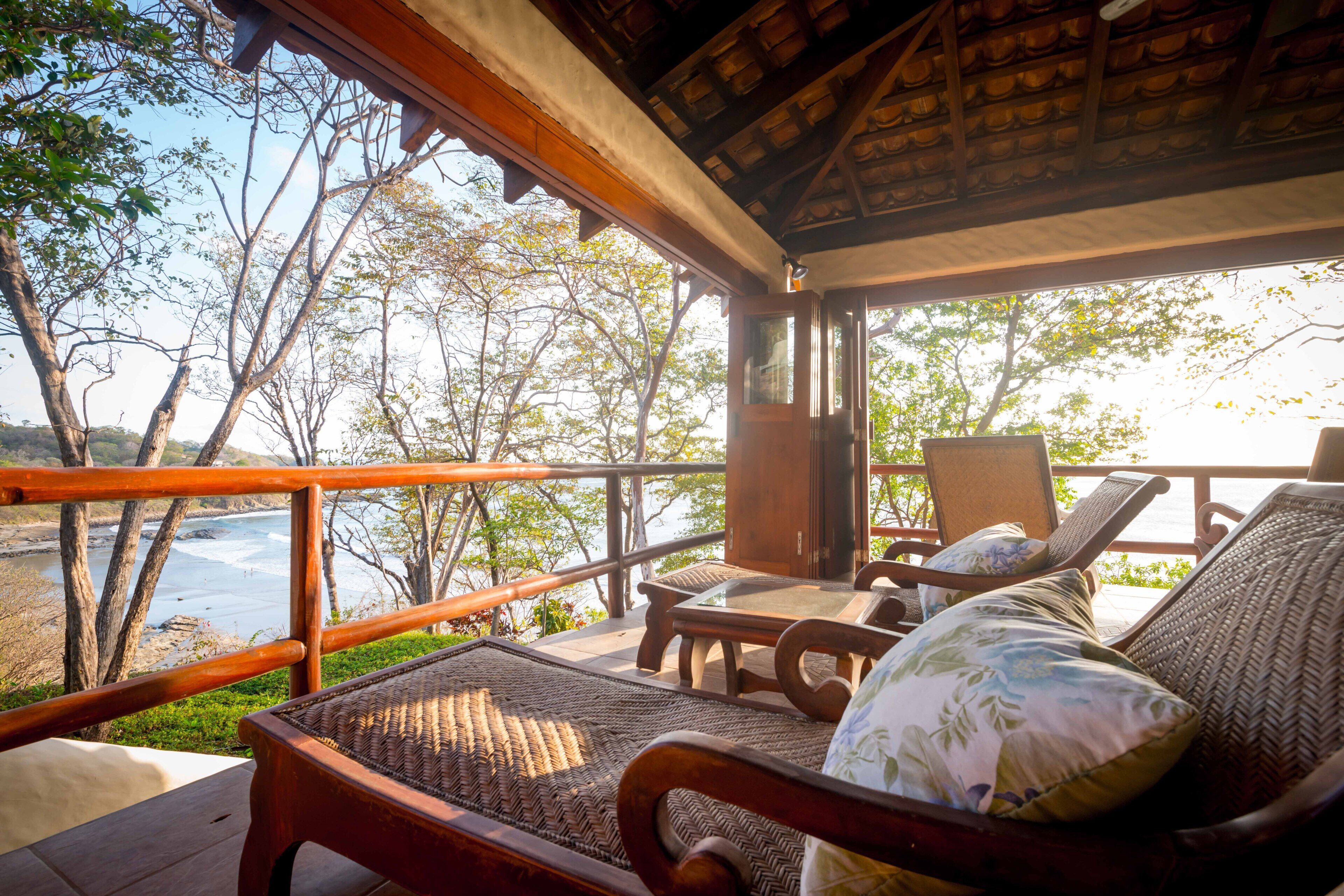 Terraza de madera con muebles de mimbre con vista a un río.