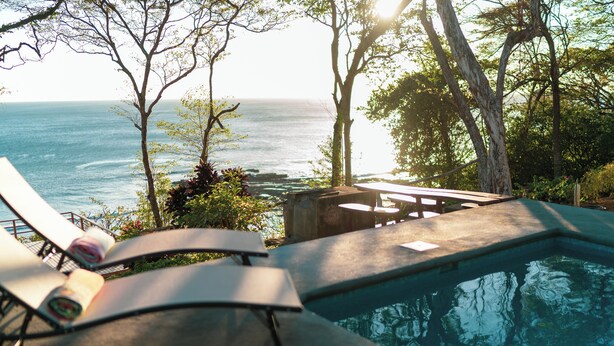 Un espace aménagé au bord de la piscine, avec des chaises longues et une vue sur l’océan.