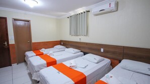 Et hotelværelse med fire senge, hver med hvide sengetøj og orange detaljer, en træsenggavl, en aircondition og en dør.