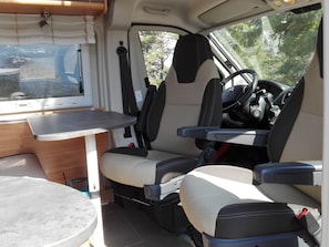 Interior compacto de vehículo con una mesa plegable, dos asientos, volante y palanca de cambios.