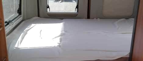 Interior compacto de una caravana con cama, una ventana pequeña y una zona de kitchenette.