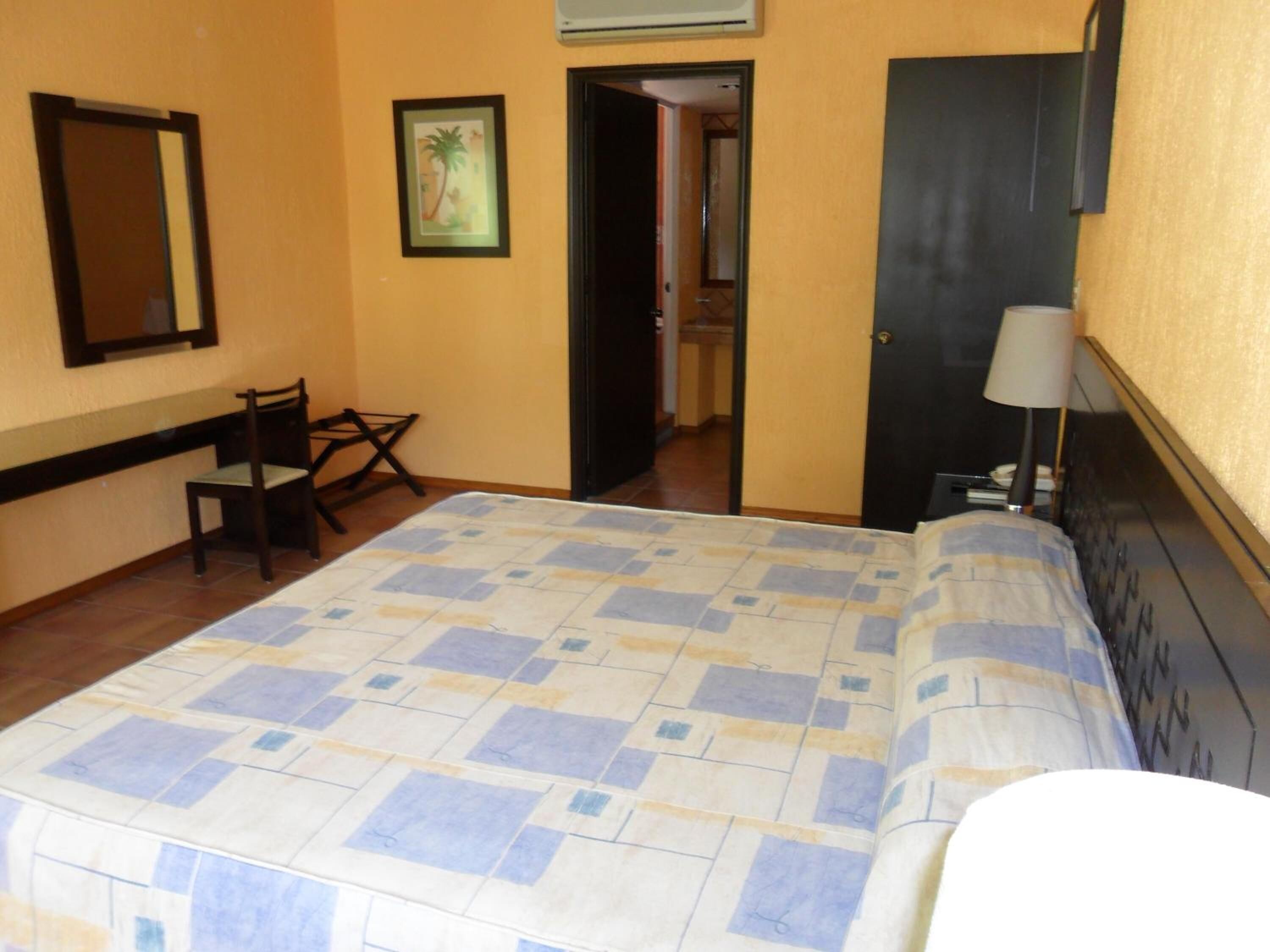 Habitación de hotel con cama, una silla, un escritorio, una puerta y un espejo.