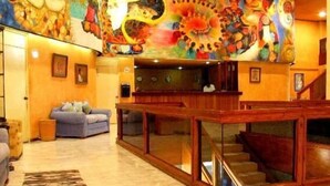A lobby with a colorful mural, a wooden reception desk, a staircase, and a seating area with a patterned rug. - Hotel Calli (Tehuantepec)