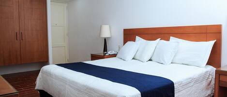 Ein Hotelzimmer mit einem großen Bett, einem Holzschrank, einem Nachttisch mit Lampe und einem Telefon.