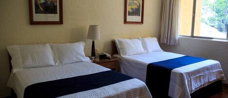 A hotel room with two beds, a nightstand with a lamp, and framed artwork on the walls.