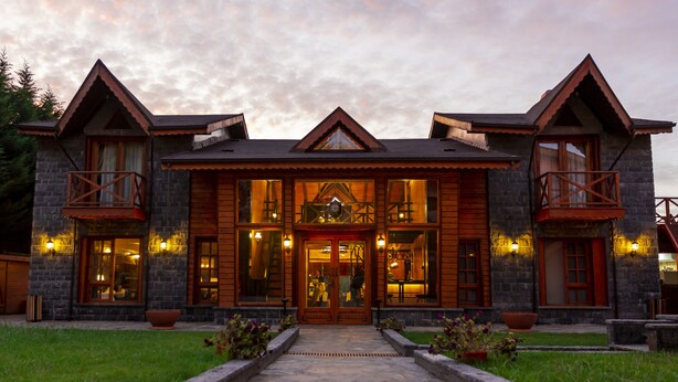 A two-story log cabin with a stone facade, large windows, and a central entrance with a decorative door. - The Swanpark Hotel (Sile)
