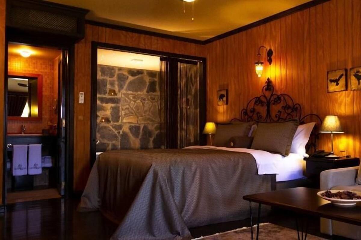 A hotel room with a bed, a sofa, a coffee table, and a stone wall.