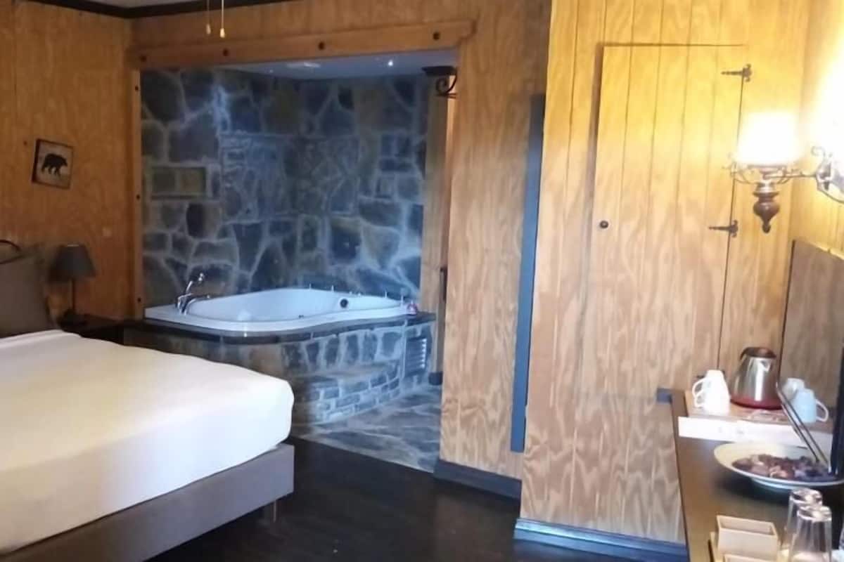 A bedroom with a large bed, a stone wall, and a bathtub.
