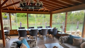 A covered outdoor seating area with a table and chairs, overlooking a body of water. - The Swanpark Hotel (Sile)