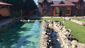 A clear swimming pool with a stone border, surrounded by a well-maintained lawn and a large stone building with multiple windows and a red roof. - The Swanpark Hotel (Sile)
