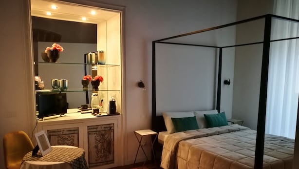 Un dormitorio con cama con dosel, una mesita de noche, un escritorio pequeño con silla y un espejo grande.