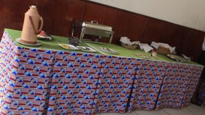 A buffet table with a patterned tablecloth, a coffee pot, and various food items. - Hôtel Beau Rivage (Douala)