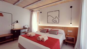 Un dormitorio con cama, mesitas de noche, escritorio, silla, lámpara y una obra de arte en la pared.