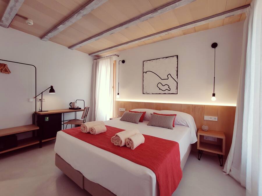 Un dormitorio con cama, mesitas de noche, escritorio, silla, lámpara y una obra de arte en la pared.