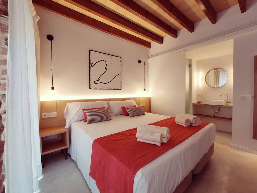 Une chambre d’hôtel avec un grand lit, un plafond en bois, une œuvre d’art accrochée au mur, une table de chevet et une salle de bain équipée d’un lavabo et d’un miroir.