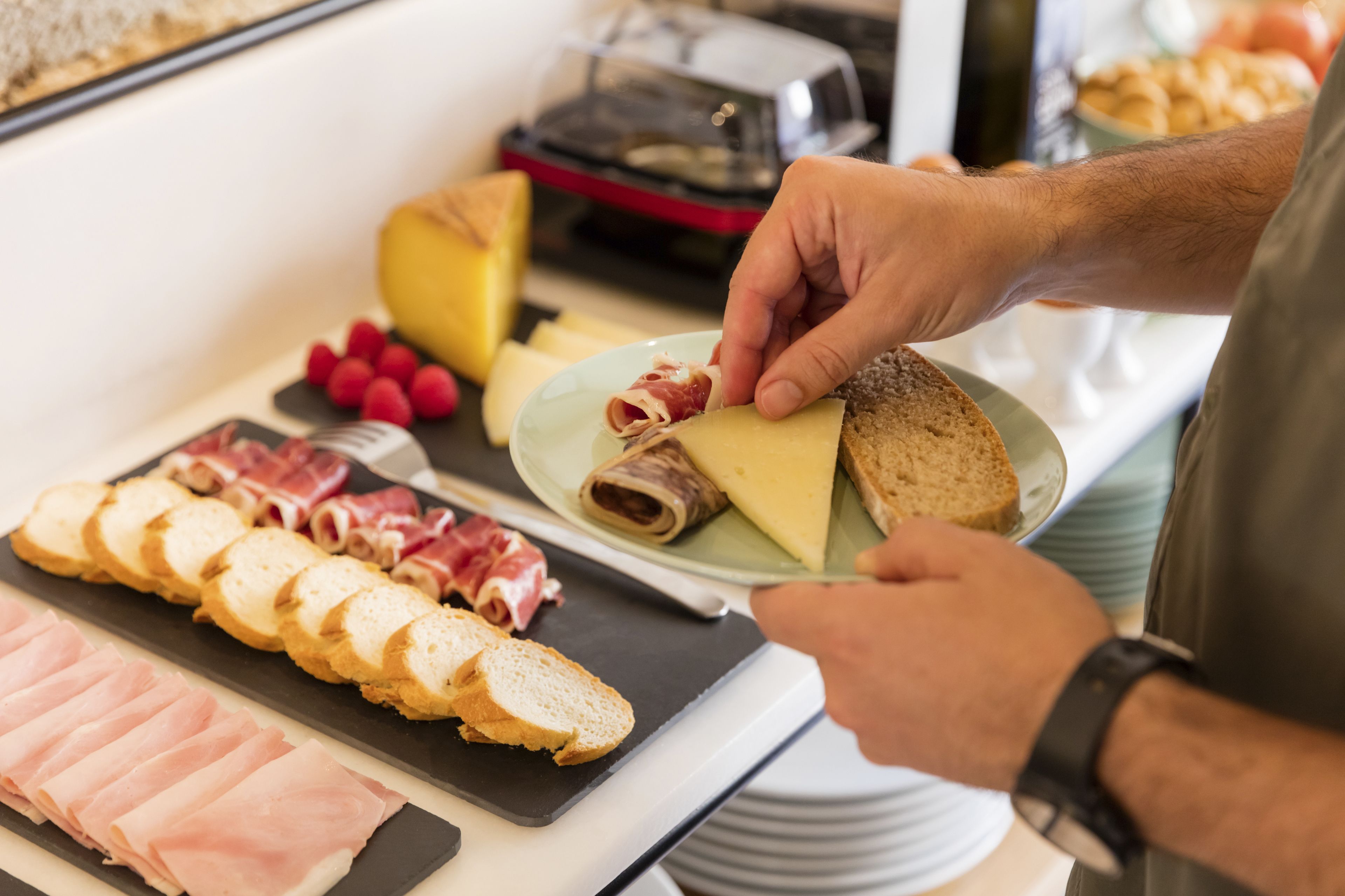 A person preparing food with various items on a table, including sliced meats, cheese, and bread.