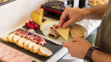 A person preparing food with various items on a table, including sliced meats, cheese, and bread.