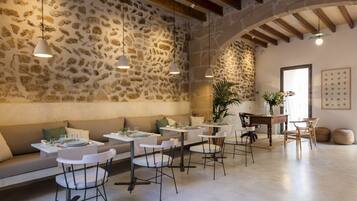A restaurant with stone walls, wooden beams, and white furniture. Tables are set with plates and glasses.