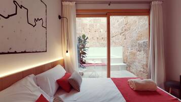 Une chambre avec un lit, une carte accrochée au mur, une vue sur le balcon extérieur et un mur en pierre.