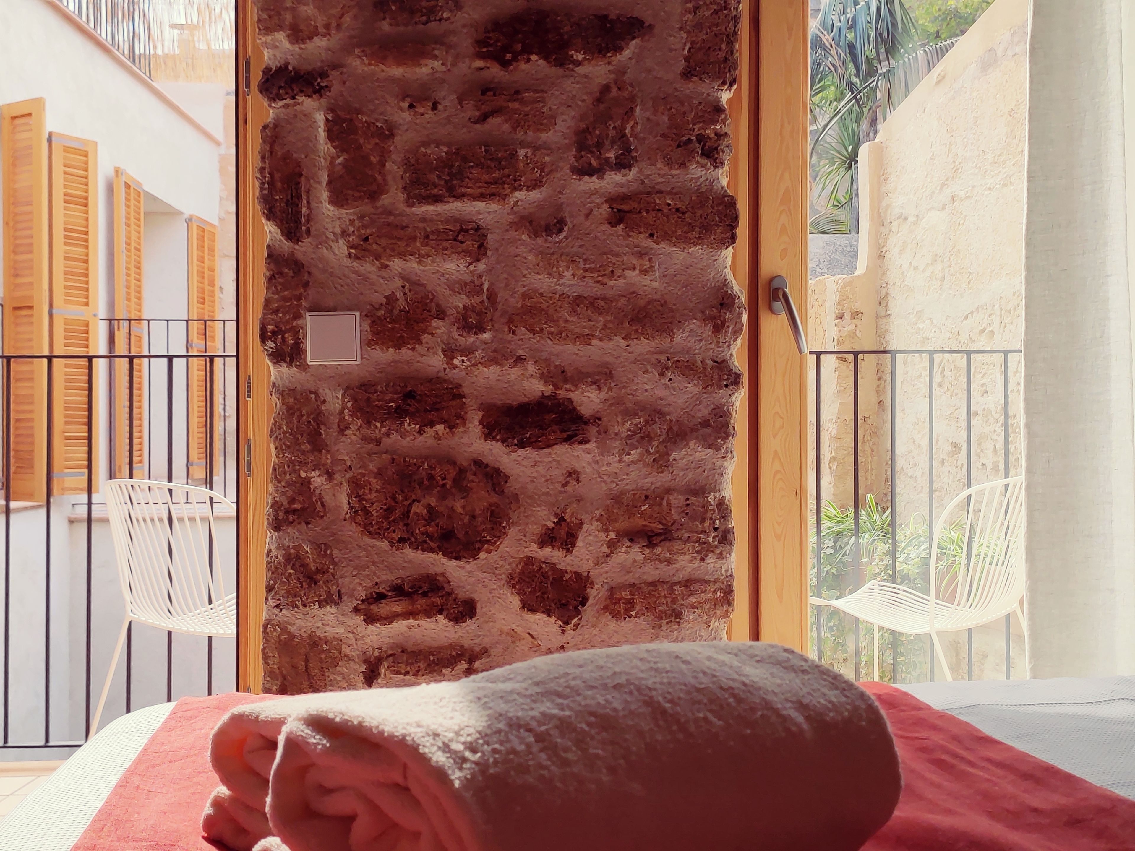 Una habitación con pared de ladrillo, puerta de madera y vistas a un balcón con sillas.