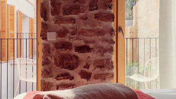 Una habitación con pared de ladrillo, puerta de madera y vistas a un balcón con sillas.