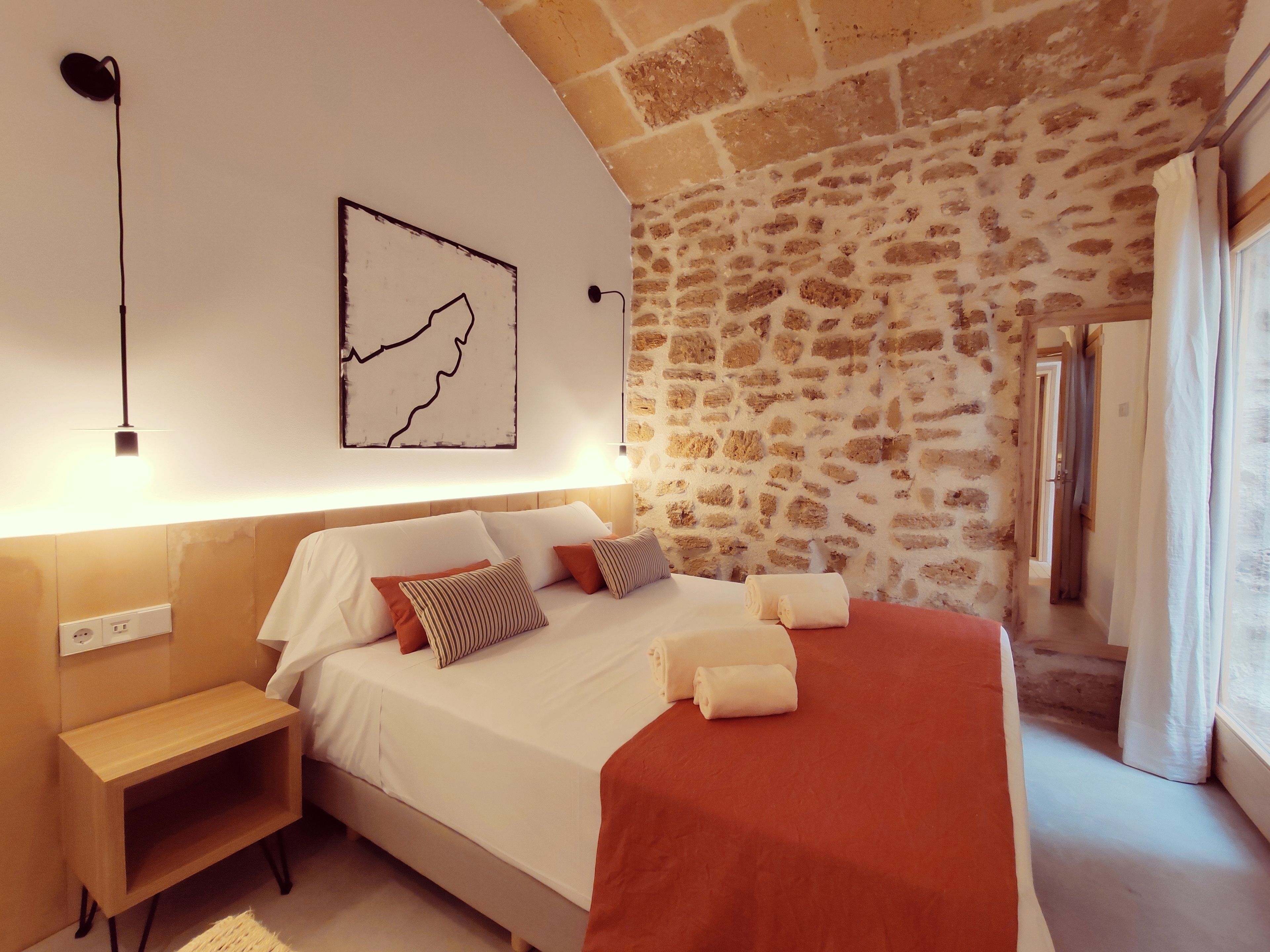 A bedroom with a stone wall, a bed with white bedding, a wooden nightstand, and a map artwork.